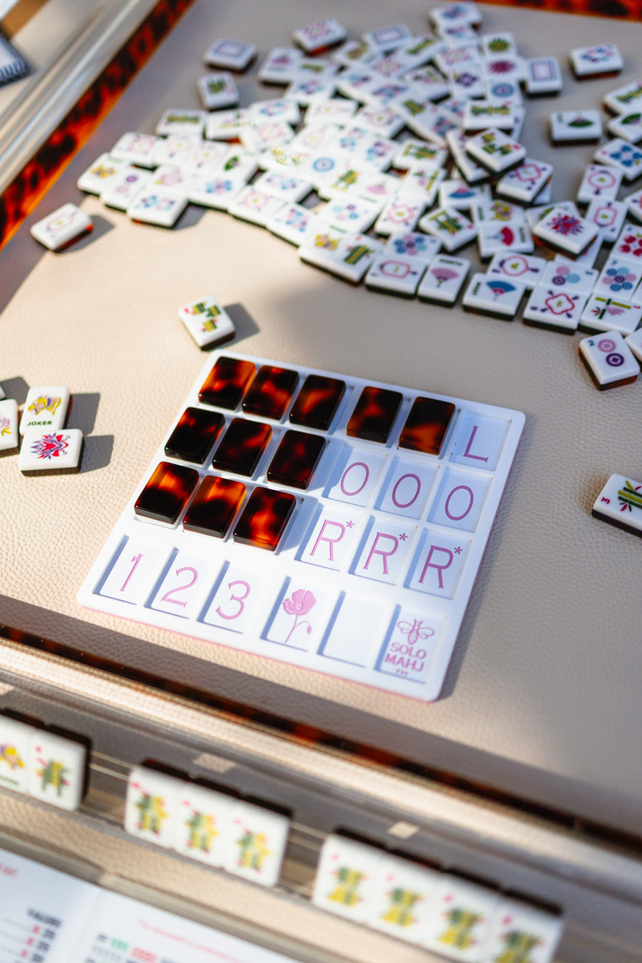 A tortoiseshell SoloMahj practice board sits amid scattered mahjong tiles, including a Joker